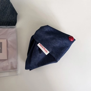 Macro detail of handmade dark blue denim pouch with red button and handmade label
