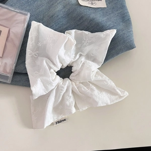 Détail d'un chouchou en coton blanc avec broderie florale et étiquette tissée