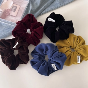 Detail view of five velvet scrunchies in wine red, black, brown, navy, and yellow colors