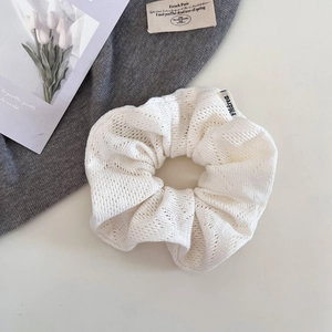 Détail d'un chouchou en maille ajourée blanche avec étiquette de marque tissée