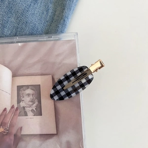 Detailed view of an oval black and white gingham hair clip with golden metal base