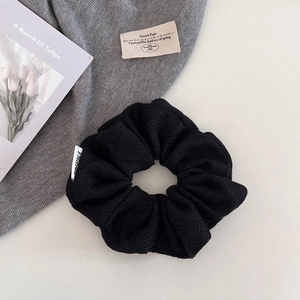 Détail d'un chouchou noir à texture plissée avec une étiquette de marque blanche
