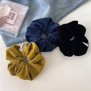 Close-up of velvet hair scrunchies in yellow, blue and black on a minimalist backdrop