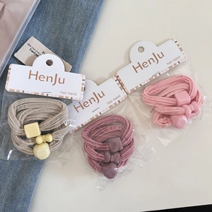 Close-up of three elastic hair bands with geometric bow charms in cream and pink tones