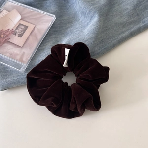 Close-up of dark brown velvet scrunchie texture with a soft sheen and elegant woven label