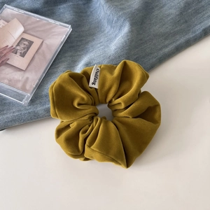 Macro detail of mustard yellow velvet scrunchie showing soft texture and woven label
