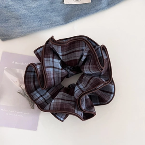 Close-up of blue and brown plaid scrunchie with pleated edges on a clean aesthetic background
