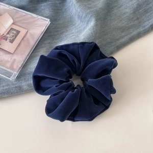 Detailed view of a dark blue velvet scrunchie on a denim and white minimalist surface