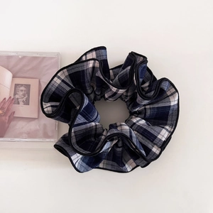 Detailed close-up of blue plaid scrunchie with black piping on white background