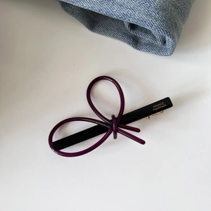 Detail of a purple resin bow hair clip with gold logo and black metal spring component