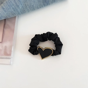 Gros plan sur un chouchou en soie noire avec un pendentif cœur bordé d'or sur blanc