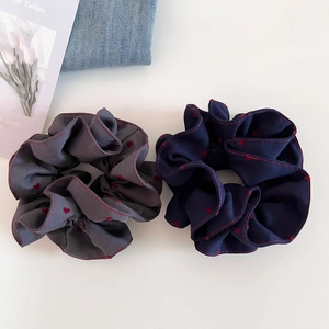 Grey and navy scrunchies with red heart patterns and stitched edges set on white surface