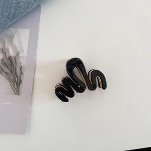 Détail d'une pince à cheveux ondulée noir et or sur un fond esthétique et élégant