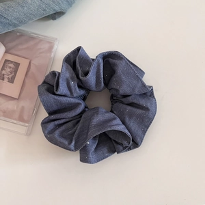 Détail d'un chouchou en denim bleu foncé orné de paillettes argentées scintillantes