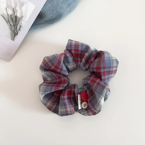 Close-up of red and blue plaid scrunchie with button accents and soft cotton fabric texture