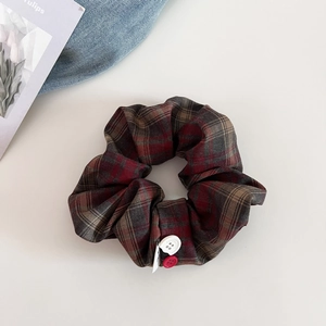 Detail of red plaid scrunchie with decorative buttons and small fabric label
