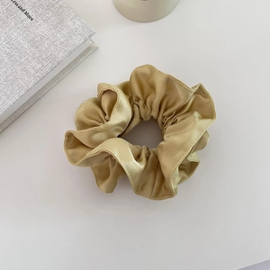 Gros plan sur un chouchou en satin doré champagne avec une texture plissée élégante