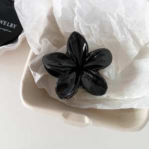 Detail of a large black glossy flower hair claw clip on a minimalist jewelry display tray