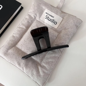 Pince à cheveux noire brillante minimaliste avec découpe en U sur un sac en lin beige