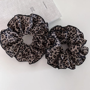Close-up of two pieces leopard print scrunchies with black piping on white surface