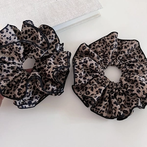 Detailed view of leopard print hair scrunchies with black piping edge on a desk