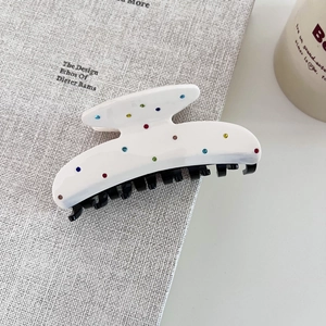 Vue détaillée de la pince à cheveux en acétate crème avec strass colorés sur un livre