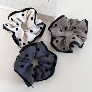 Detail of three polka dot scrunchies with satin edges in white, light gray, and dark gray