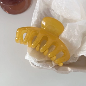 Macro shot of a glossy ginger yellow resin hair claw clip on soft white textured paper