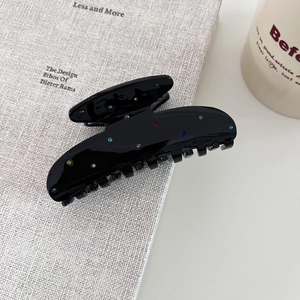 Détail macro d'une grande pince à cheveux noire en acétate ornée de strass multicolores