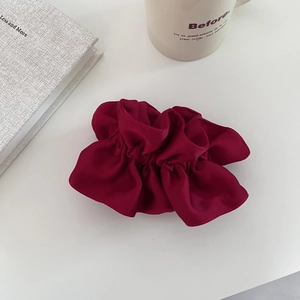 Gros plan d'un chouchou en satin bordeaux avec des plis doux sur un bureau minimaliste