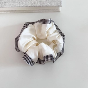 Detail view of cream satin scrunchie with elegant black and white plaid trim texture