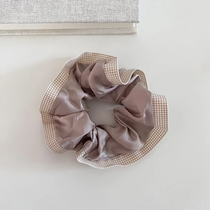 Detail of beige checkered and taupe satin scrunchie on a white minimalist background