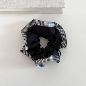 Detail view of a black satin scrunchie with houndstooth plaid pattern edges and texture