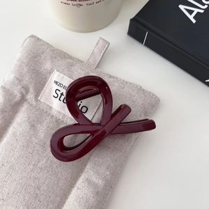 Elegante pinza per capelli rosso bordeaux con nodo infinito su sfondo in tessuto crema