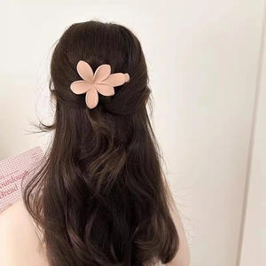 Eleganter mattrosa Blumen-Haarclip an einem Modell mit langen braunen Wellen