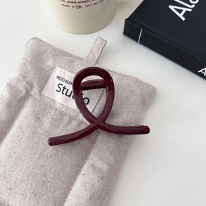 Dettaglio di una pinza per capelli in resina bordeaux con design incrociato su sfondo