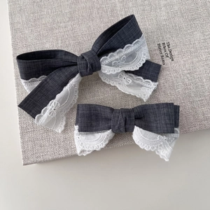 Set of two gray bow hair clips with white lace trim on a minimalist background