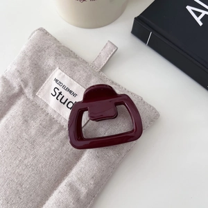 Dettaglio di un fermaglio per capelli geometrico rosso scuro su borsa in lino grigio