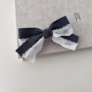Grey fabric bow hair clip with white lace trim on a book for a minimalist aesthetic
