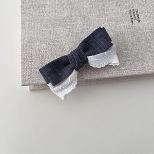 Detail of grey denim and white lace bow hair clip on a textured book surface