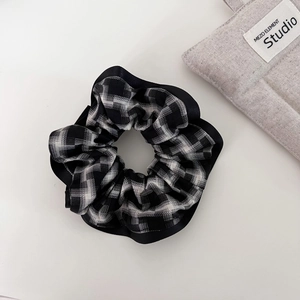 Close-up of black and white plaid fabric scrunchie with smooth black edge on a white surface