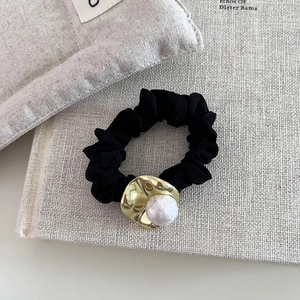 Chouchou noir avec métal doré irrégulier et perle sur un fond minimaliste élégant