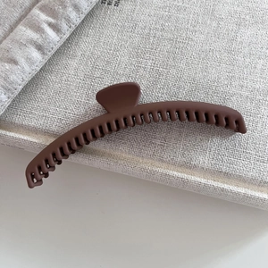 Detailed view of large matte brown hair claw clip with dense teeth on textured fabric