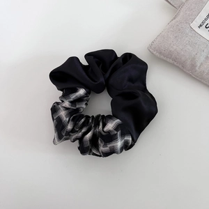 Detail of a two-tone scrunchie featuring black satin and monochrome plaid fabric texture