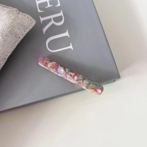 Vue détaillée de la barrette en acétate avec texture marbrée rose et verte sur un livre