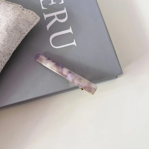 Détail d'une barrette baguette en acétate marbré violet avec base en métal doré brillant