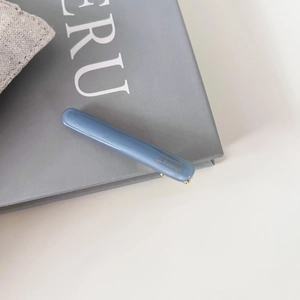 Vue rapprochée d'une pince à cheveux en acétate bleu Morandi avec logo doré