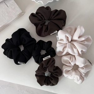 Three elegant corduroy hair scrunchies in black, brown and cream on a minimalist background