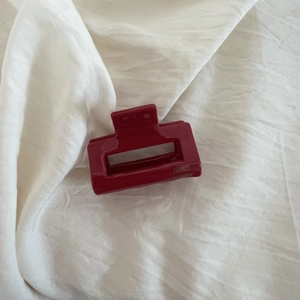 Détail d'une pince à cheveux rectangulaire rouge foncé évidée sur tissu blanc doux
