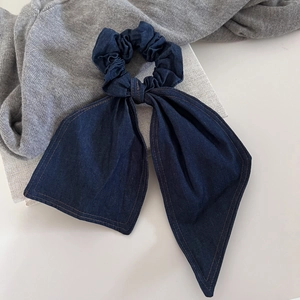 Large dark blue denim bow hair tie with contrast stitching on a textured fabric background